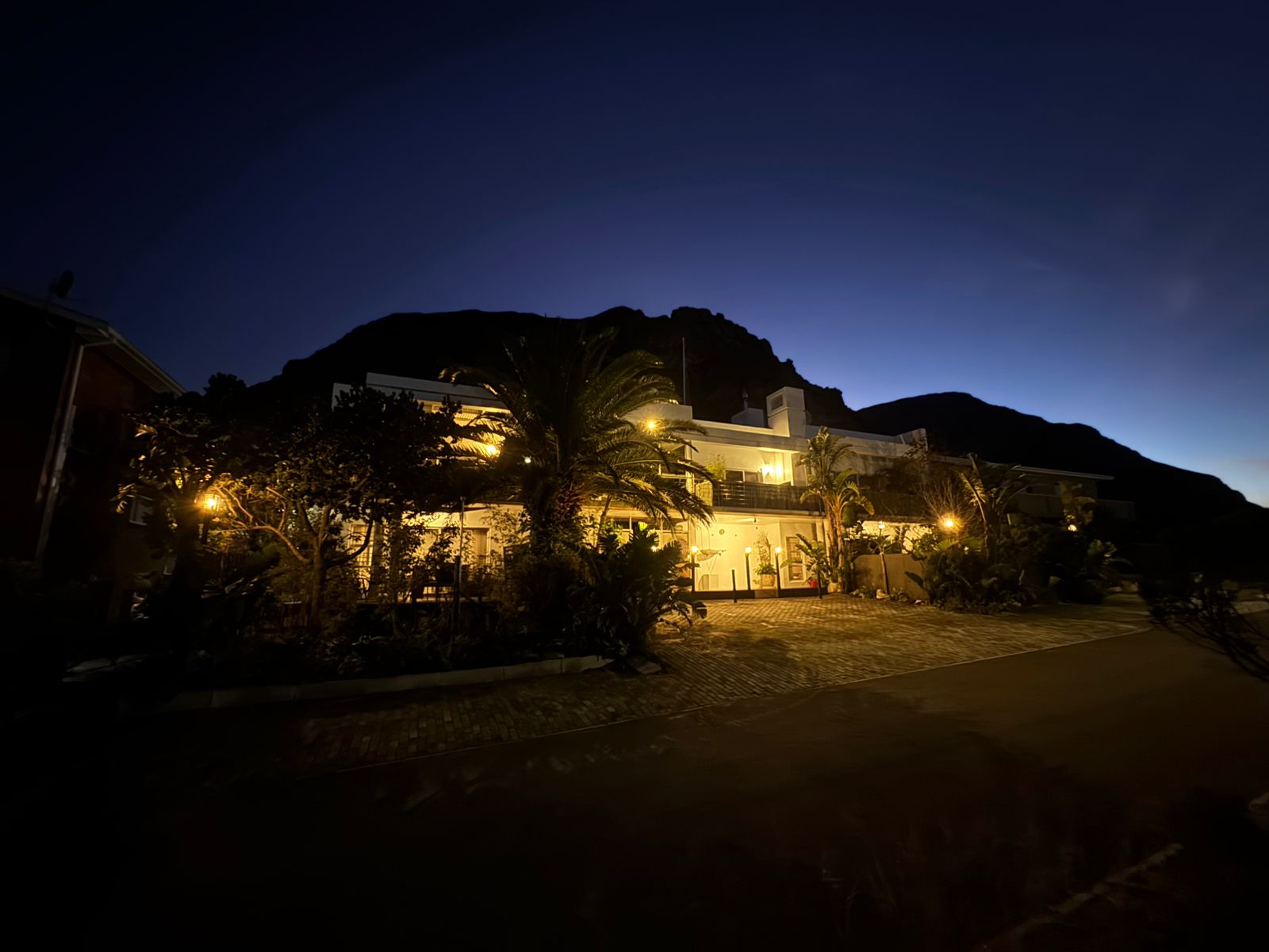 78 on 5th at dusk — illuminated gardens, palm trees, mountain silhouette, Voelklip Hermanus